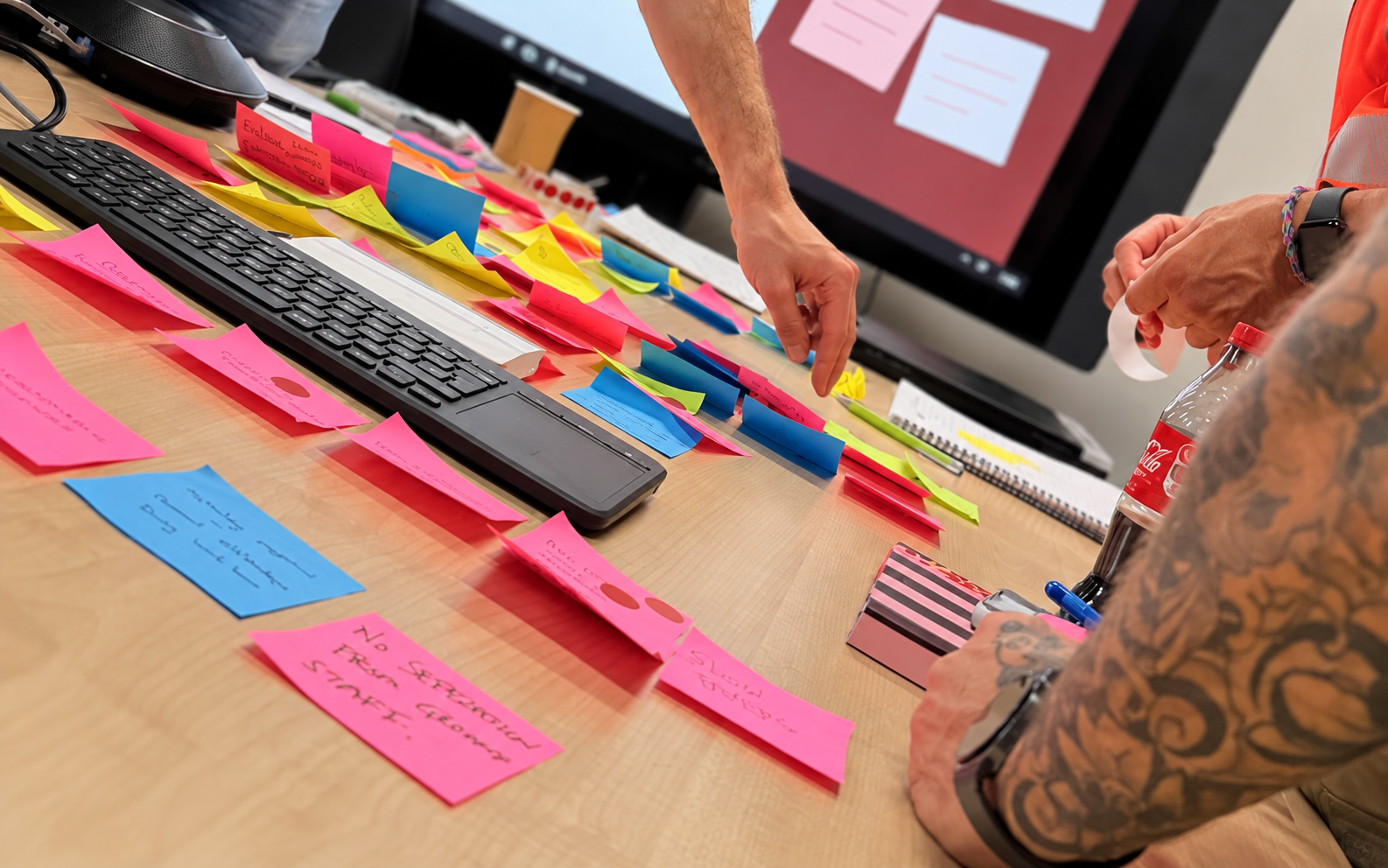 Hands arranging handwritten sticky notes on a workshop table, with voting dots marking selected ideas.